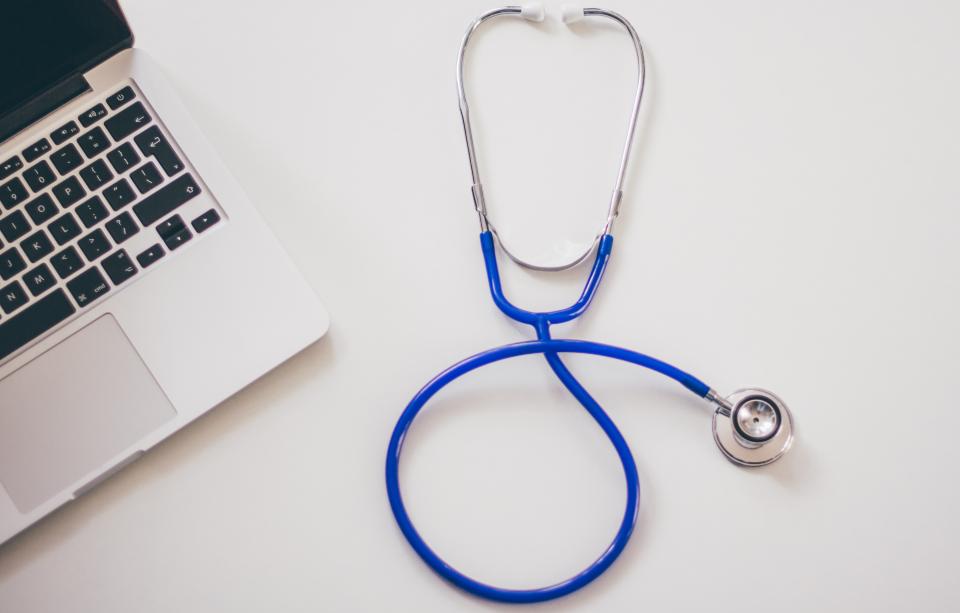 Stethoscope on a white desk next to a laptop