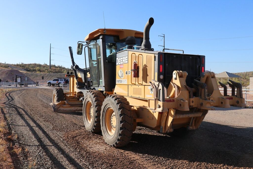 Road grader working a dirt site under blue sky